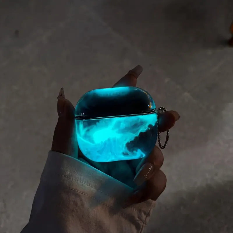 Electric Blue LumiCases AirPods cover glowing bright cyan-blue in the dark, held in a hand with its keychain